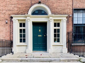 A traditional brick building with a green door, white columns, and a small balcony with a metal railing. - Leevin Hostel George (Dublin)