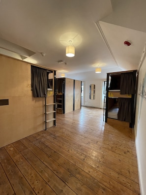 A spacious room with wooden flooring, a bunk bed, a ladder, and a mirror on the wall.