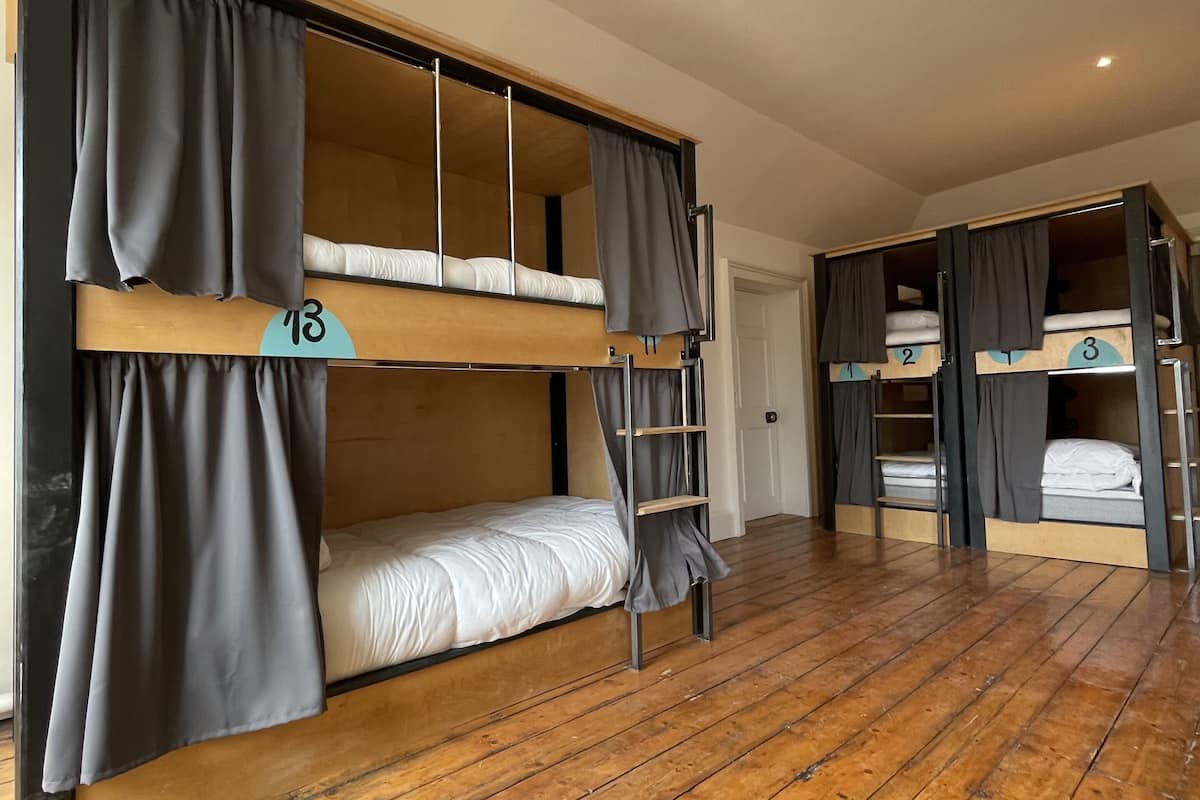 Un dormitorio con literas, suelo de madera y cortinas.