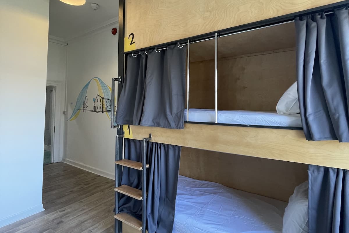 Habitación con literas, cabecera de madera, una escalera y un estante pequeño.