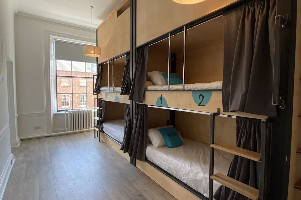 Un dormitorio con literas, una ventana que da a un edificio de ladrillo y un radiador.