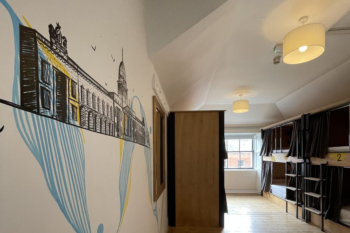 Un pasillo con suelo de madera, literas y un mural en la pared.