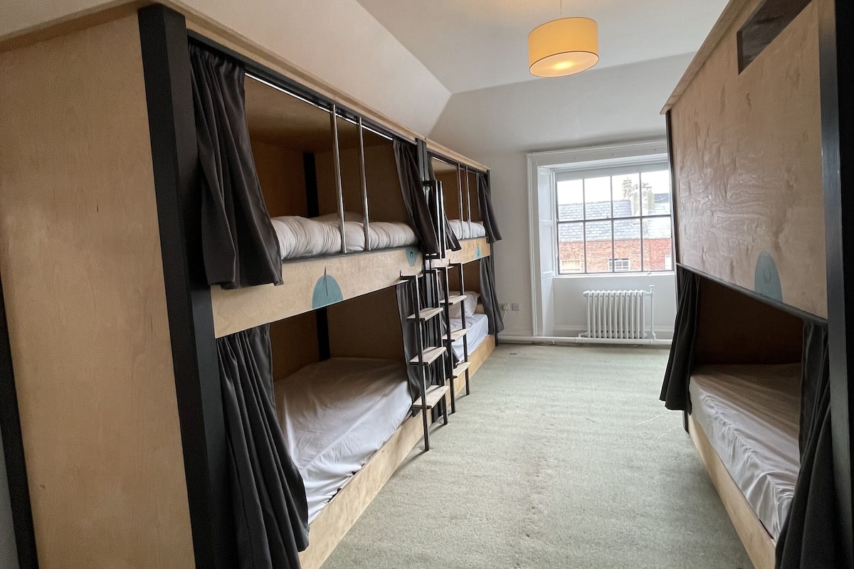 Habitación tipo dormitorio con literas, un radiador y una ventana con vistas a edificios.