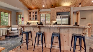 Una cocina con armarios de madera, una isla central con taburetes y suelo de piedra.