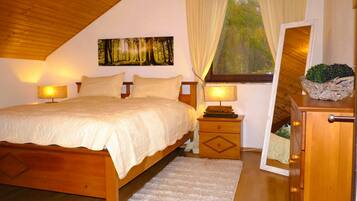 A bedroom with a wooden bed, a nightstand with a lamp, a dresser, a window with curtains, and a painting on the wall.