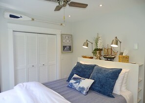 A bedroom with a bed, a ceiling fan, a wall-mounted ship model, and a framed picture.