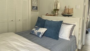 A bedroom with a bed, a ceiling fan, a ship model, and a framed book on the wall. - Waterfront Condo-fully renovated, in the desirable West End, steps to the beach. (Provincetown)