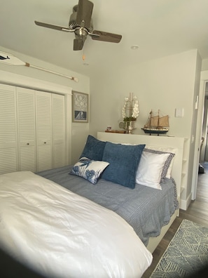 A bedroom with a bed, a ceiling fan, a ship model, and a framed book on the wall.