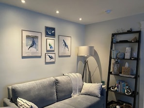 Una sala de estar con un sofá gris, una lámpara de pie y obras de arte colgadas en la pared.