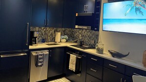 Een moderne keuken met donkere kastjes, een ingebouwde oven, een magnetron en een grote flatscreen televisie aan de wand.