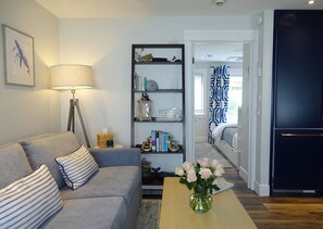 A living room with a sofa, a lamp, a bookshelf, and a vase with flowers.