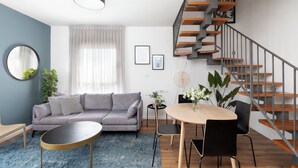 A modern living room with a grey sofa, round coffee table, and a staircase with wooden steps and metal railings. - AirTLV - Arlozorov Apartment's (Ramat Gan)
