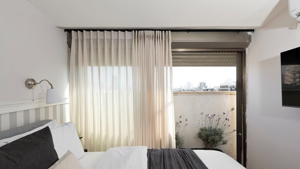 A hotel room with a bed, a window with curtains, a city view, and a potted plant. - AirTLV - Arlozorov Apartment's (Ramat Gan)