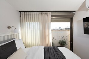 A hotel room with a bed, a window with curtains, a city view, and a potted plant.