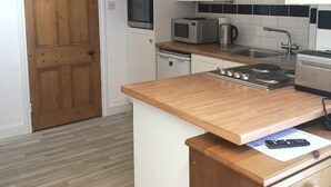 A compact kitchen with white cabinets, a wooden countertop, a microwave, a kettle, and a stove. - Charming 1-bedroom Apartment Near Hailsham (Hailsham)