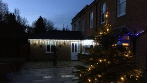 A brick building with a covered patio area, a Christmas tree with lights, and a small garden. - Charming 1-bedroom Apartment Near Hailsham (Hailsham)