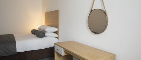 Une chambre à coucher avec un lit, une table de chevet et un miroir rond accroché au mur.