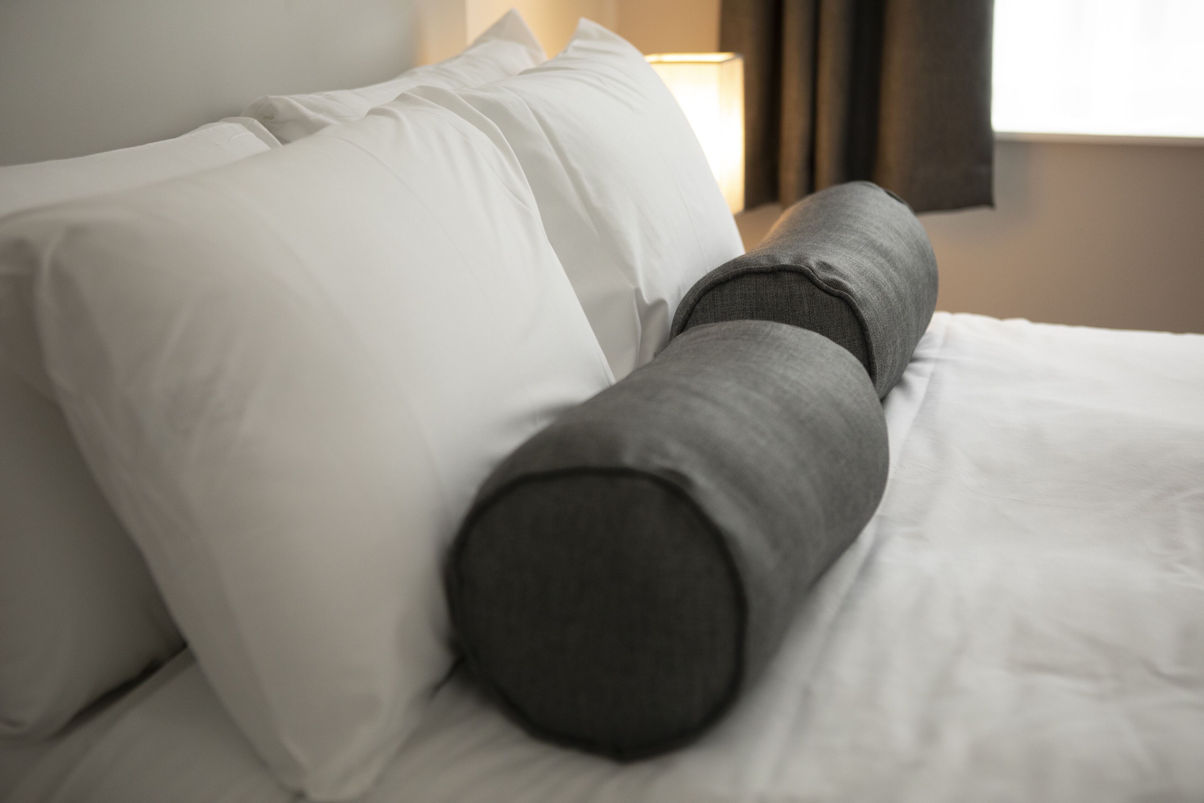A bed with white and gray bedding, a lamp, and a window with curtains.