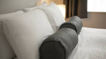 A bed with white and gray bedding, a lamp, and a window with curtains.