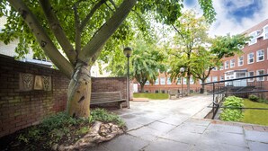 A courtyard with a bench, a tree, and a brick wall. - Wellington Apartments (Norwich)