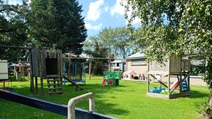 Een speeltuin met diverse speeltoestellen, waaronder een glijbaan en schommels, omgeven door een hek.