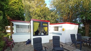 Een stacaravan met een klein terras, inclusief buitenmeubels en een tafel.