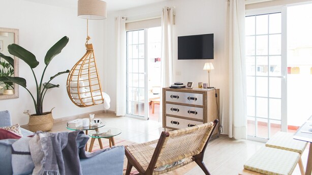 Een lichte woonkamer met een hangstoel, een glazen tafel, een bank en een televisie aan de muur.