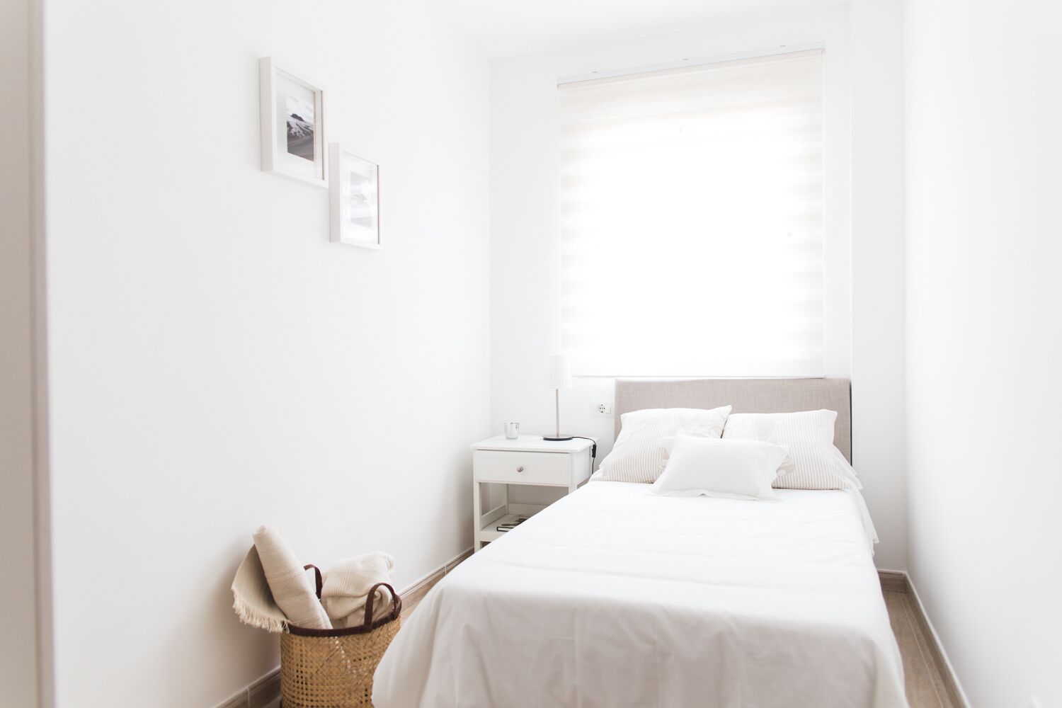 Une chambre à coucher au style minimaliste, avec un lit, une table de chevet et un panier rempli de serviettes.
