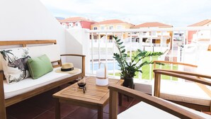 Een balkon met een houten tafel, een comfortabele bank en een bloempot.