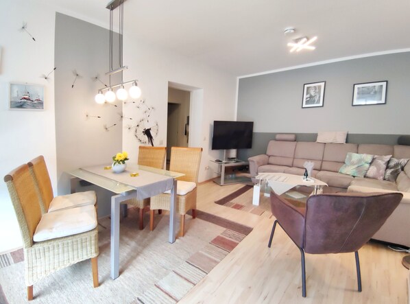 Un salon moderne comprenant un canapé, une table à manger avec des chaises, un téléviseur et des œuvres d’art décoratives au mur.