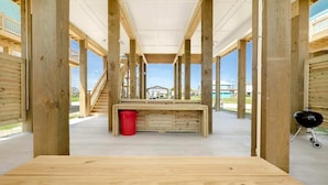 A wooden deck with a central table, a red bucket, and a barbecue grill. - Crystal Sands - 3 bedroom, 2 bath home that sleeps 8 - Easy Beach Access! (Crystal Beach)