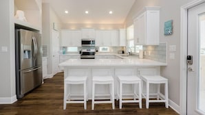 A modern kitchen with white cabinetry, a stainless steel refrigerator, a central island with bar stools, and a microwave. - Crystal Sands - 3 bedroom, 2 bath home that sleeps 8 - Easy Beach Access! (Crystal Beach)