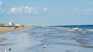 A beach with waves, people, and buildings in the background. - Crystal Sands - 3 bedroom, 2 bath home that sleeps 8 - Easy Beach Access! (Crystal Beach)