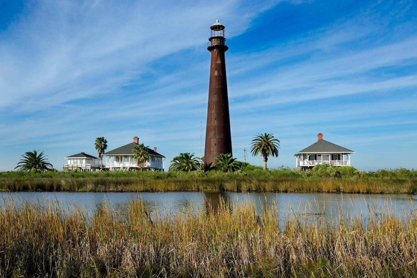 A lighthouse with two white houses on stilts, surrounded by water and vegetation.