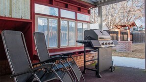 A covered patio with a grill, chairs, and a view of a backyard. - Charming cozy cottage on historic numbered streets (Idaho Falls)