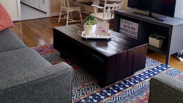 A living room with a dark wooden coffee table, two grey sofas, a colorful rug, and a TV on a stand. - Charming cozy cottage on historic numbered streets (Idaho Falls)