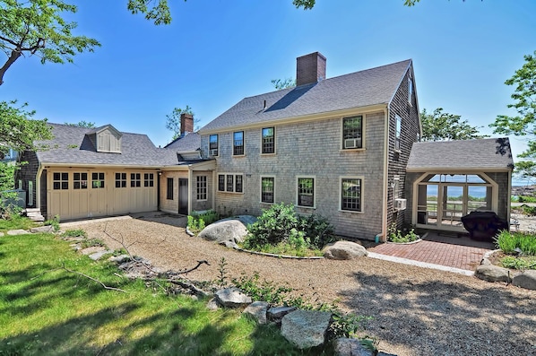 A two-story house with a covered garage, a large front yard with rocks and plants, and a view of the ocean.