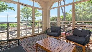 Une véranda avec de grandes fenêtres, des fauteuils en osier et une table en bois.