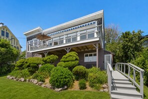 A modern two-story house with a balcony, surrounded by well-maintained gardens and a clear sky.