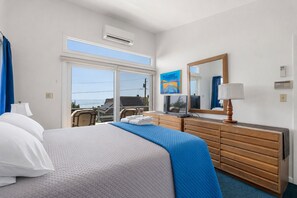 A hotel room with a bed, a dresser, a television, and a window with a view of the sea.