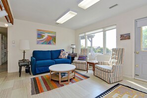 A living room with a blue sofa, a patterned armchair, a round coffee table, and a colorful striped rug.