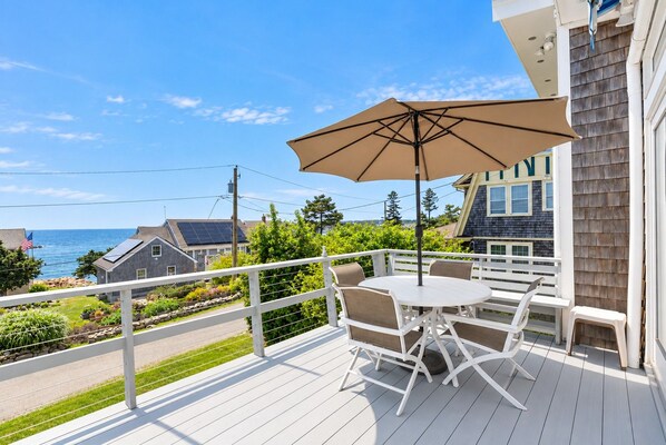 A deck with a table and chairs, a large umbrella, and a view of the ocean.