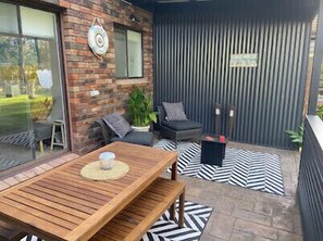 Une terrasse avec une table et des chaises en bois, une plante en pot et un tapis à rayures.