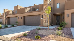 A modern multi-story building with a flat roof, a stone accent wall, and a small garden area with gravel and plants.