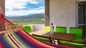 Een balkon met een hangmat, groene stoelen, een houten tafel en een lantaarn.