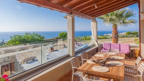 Ein Balkon mit Holztisch und Stühlen, Blick aufs Meer und eine Palme.