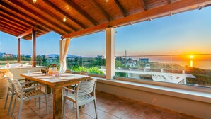 Ein Essbereich mit Holztisch und Stühlen, große Fenster mit Blick auf Sonnenuntergang und Landschaft.
