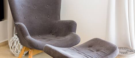 Un fauteuil à revêtement gris, avec des pieds en bois et un pouf assorti.
