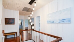 Una escalera con barandillas de madera que conduce a un piso superior, paredes con paneles blancos y un cuadro grande de paisaje.