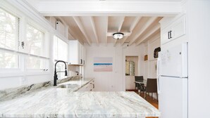 Una cocina con armarios blancos, encimera de mármol y techo de madera.
